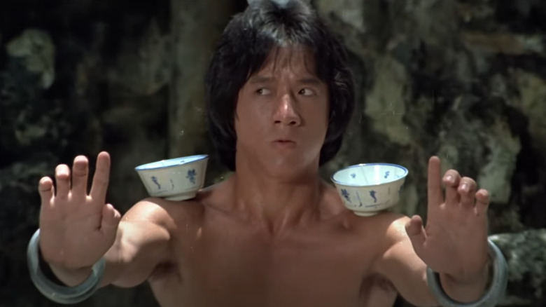 Wong Fei-Hung (Jackie Chan), in a fighting stance, balancing teacups on his head and arms in Drunken Master