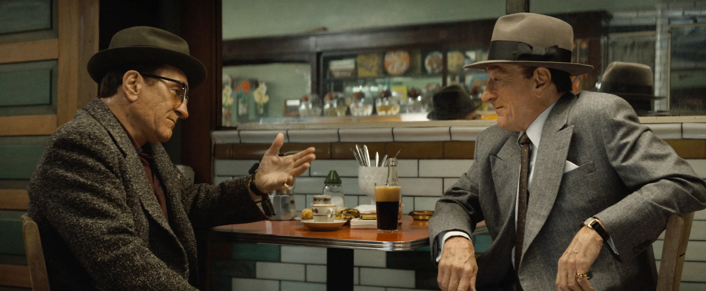 Two old men, both played by Robert De Niro, sit across from one another at a table in a restaurant in The Alto Knights.