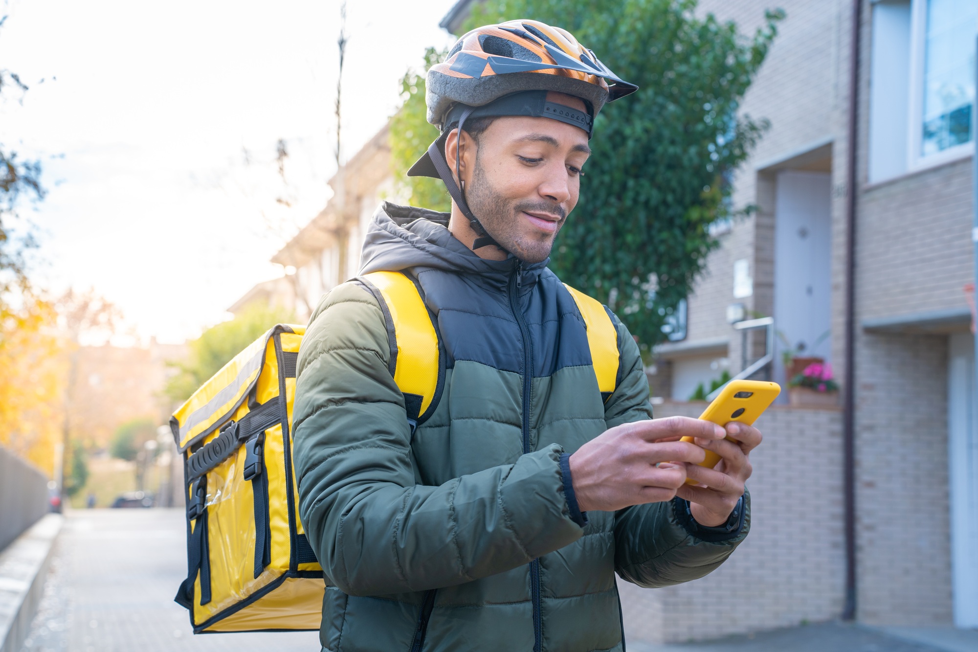 Food delivery concept. African American driver with backpack looking smartphone to deliver products