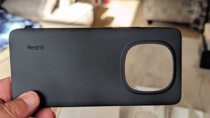 A hand holding a matte black phone case featuring the 'Redmi' logo, designed for the Redmi Note 14+ Pro 5G, with a cutout for the camera module.