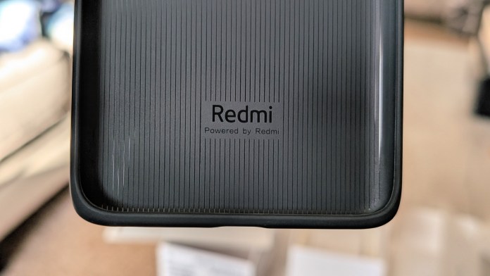 Close-up of the Redmi logo on a textured black surface, indicating the device is powered by Redmi.