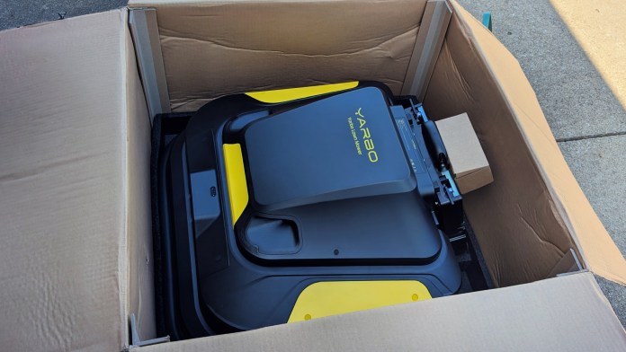 A Yarbo Core modular yard robot inside an open cardboard box, showcasing its sleek design and bright yellow accents.