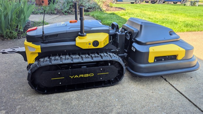 A modular yard robot named Yarbo Core, featuring a tracked base and attachments for snow blowing, lawn mowing, and leaf blowing, displayed on a concrete surface.
