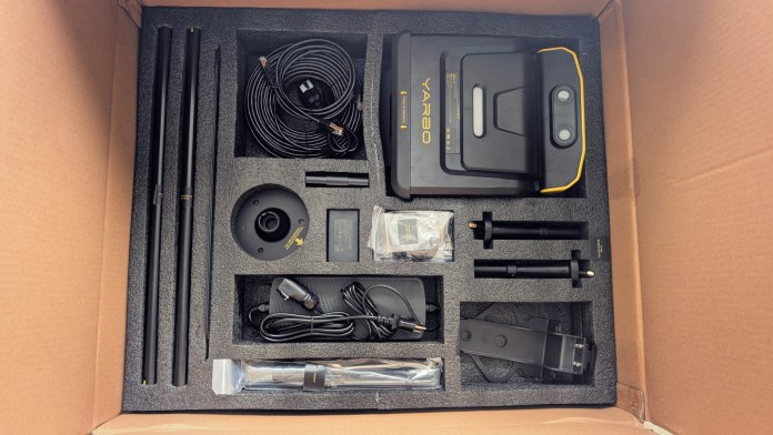 Inside a cardboard box containing the Yarbo Core modular yard robot, featuring various components including the robot base, cables, antennas, and a docking station.