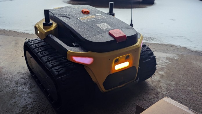 Modular yard robot, the Yarbo Core, equipped with sensors, tracked wheels, and a waterproof body, parked on a snowy surface.