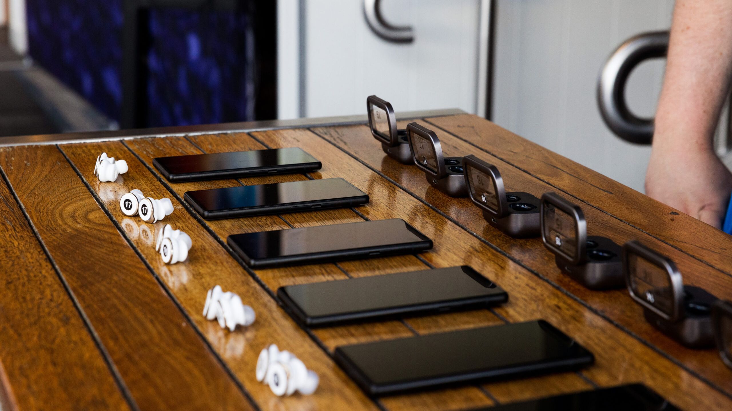 Photo of several phones and earbuds laying on a wooden surface to demonstrate Auracast capabilities.