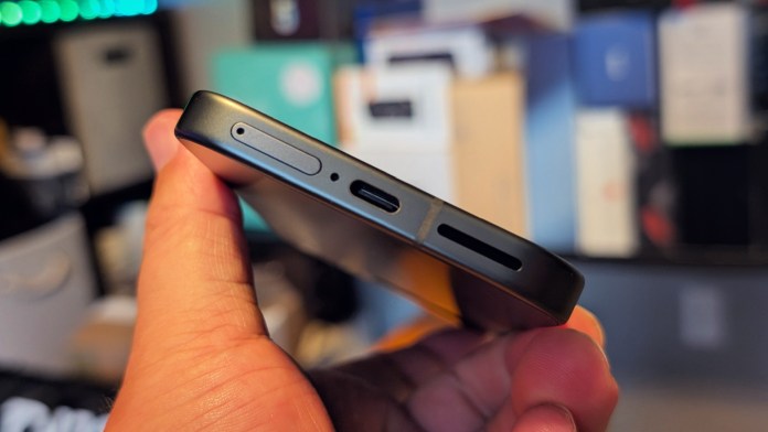 Close-up view of the Google Pixel 9A smartphone held in hand, showcasing its side profile with a SIM card slot, USB-C port, and speaker grill.