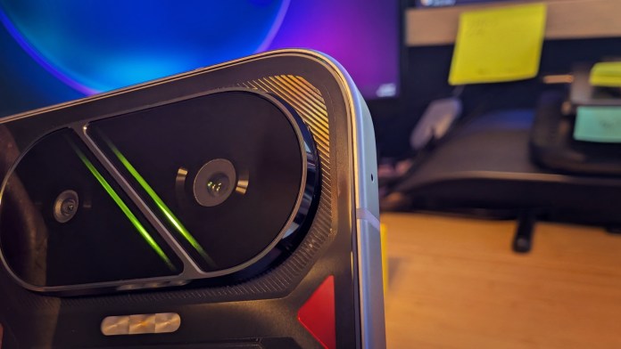 Close-up of the rear camera module of the POCO F7 smartphone, highlighting its dual-camera design and distinct features, set against a blurred office background.