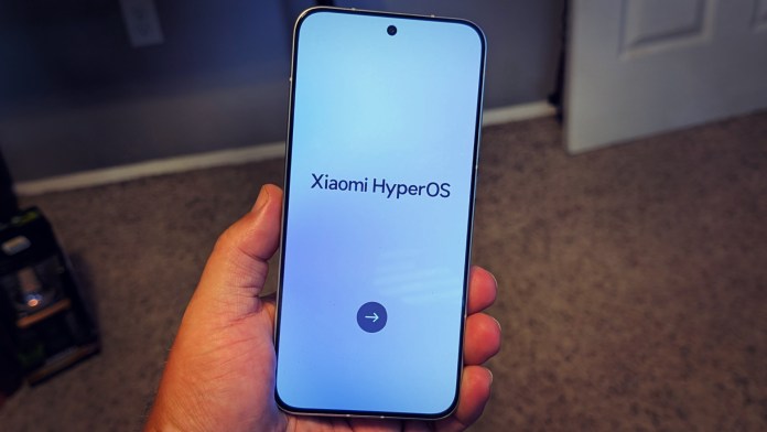 A hand holding a smartphone displaying the Xiaomi HyperOS startup screen.
