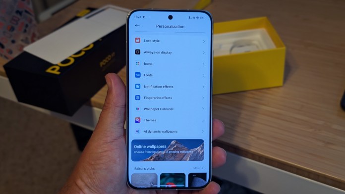 A person holding a smartphone displaying the personalization settings screen, including options like Lock style, Always-on display, Icons, Fonts, and Themes, with a POCO F7 box in the background.