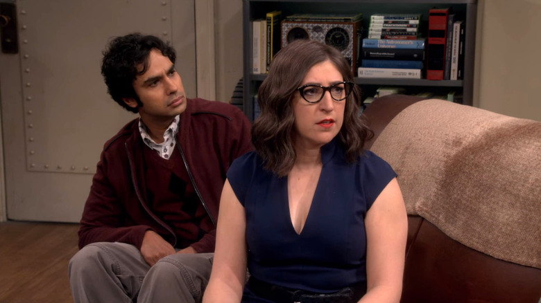 Amy sitting on the couch after her makeover with Raj behind her on The Big Bang Theory