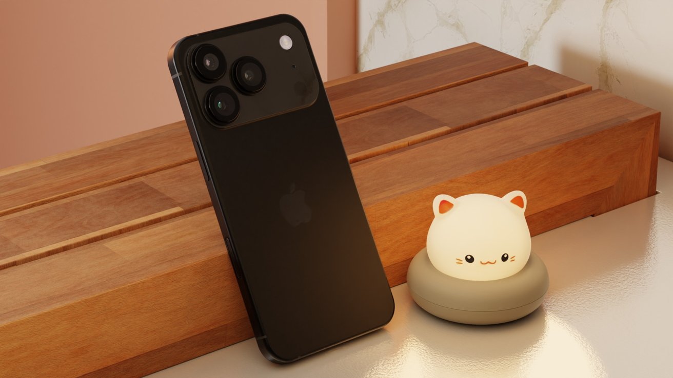 A black smartphone with three camera lenses stands on a wooden surface next to a cute, glowing cat-shaped night light.