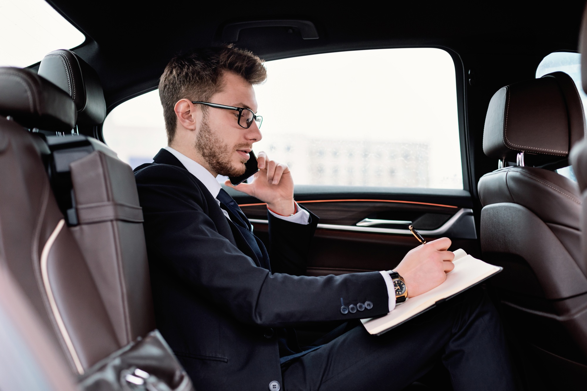 Businessman writing in notebook in luxury car