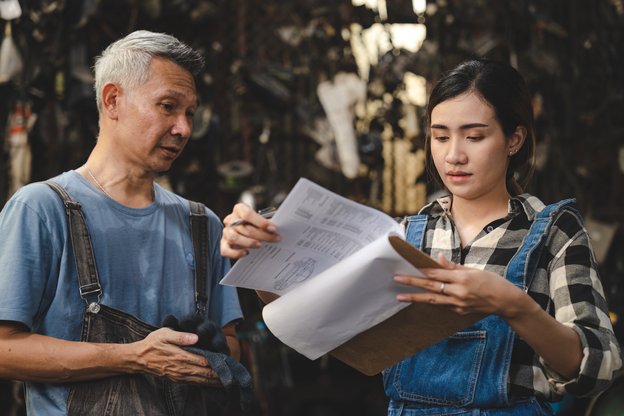 mechanic technician in uniform reading or writing document and standing in auto repair garage
