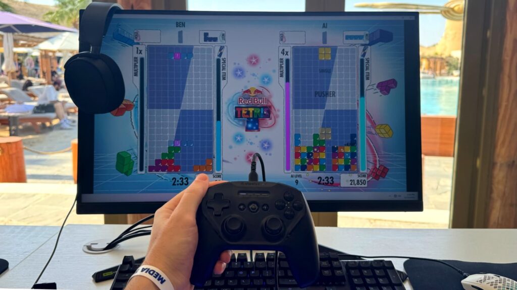 A player holds a controller while competing in Red Bull Tetris on a large screen by the poolside