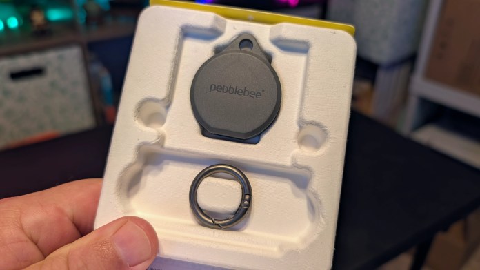 Image of a Pebblebee Clip 5 Bluetooth tracker and keyring holder displayed in its packaging, held in a person's hand.